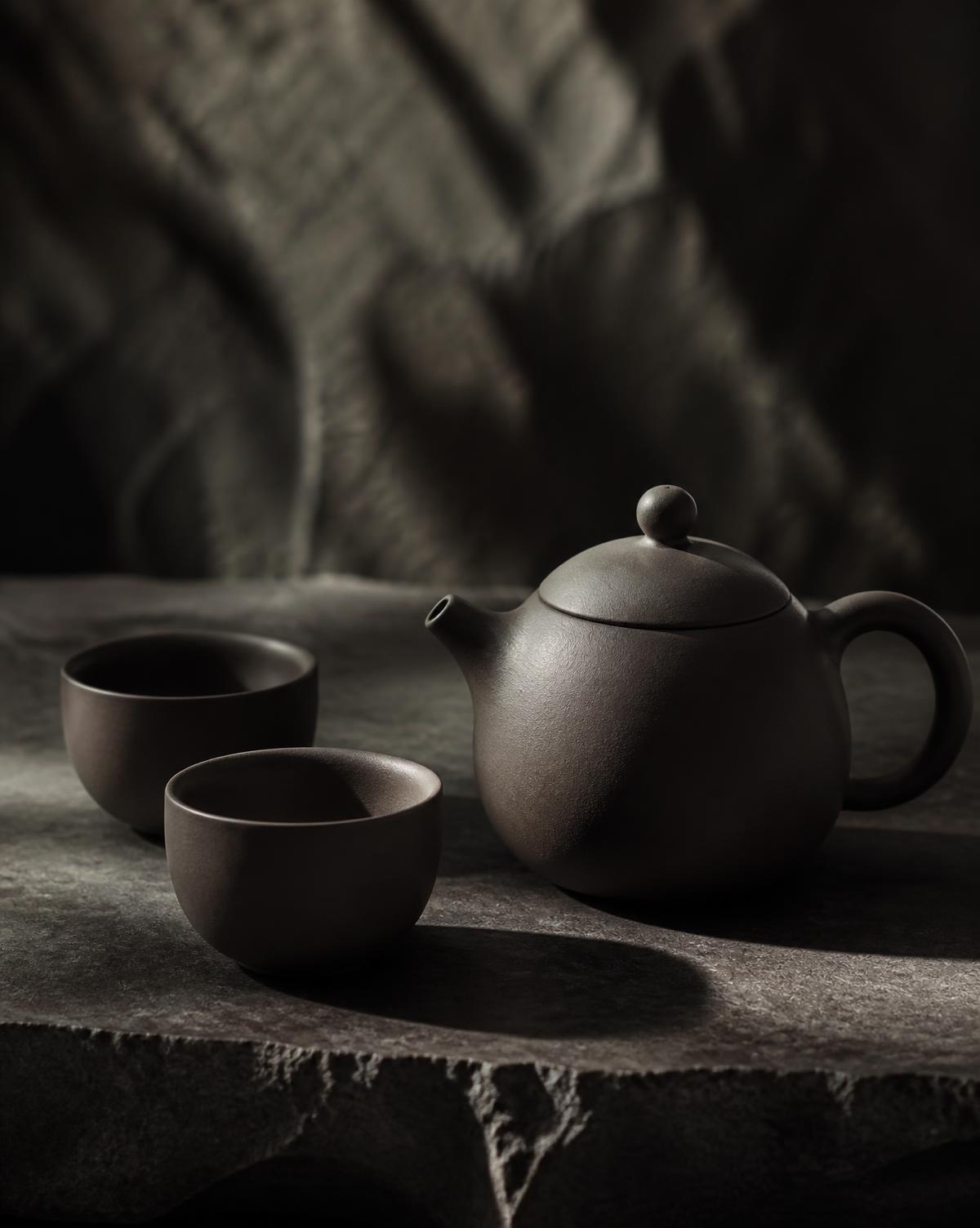 Dark clay teapot and cups on stone